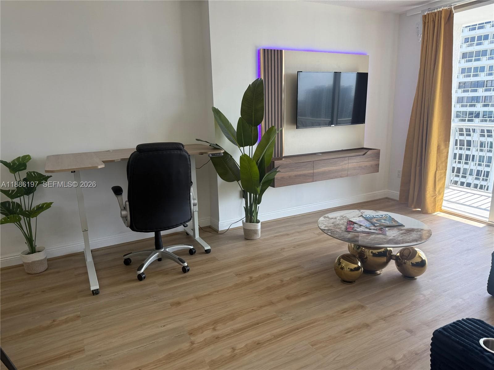 Wood-finish flooring, custom wall-mounted media console, integrated accent lighting, and balcony access