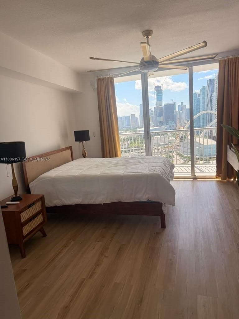 Spacious bedroom with wood-finish flooring, ceiling fan with integrated lighting, and floor-to-ceiling sliding glass doors opening to a private balcony