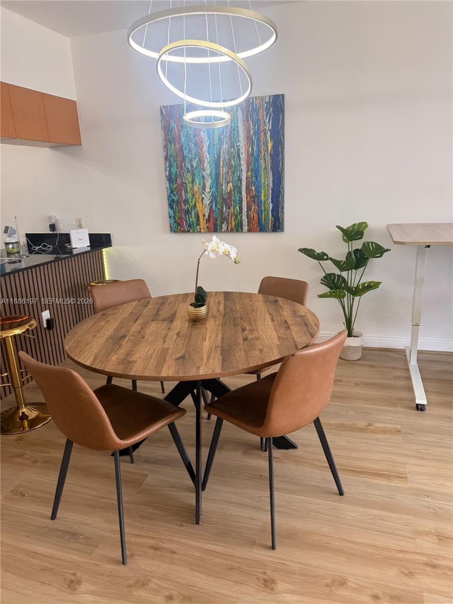 Modern dual-ring circular pendant light, vertical wood-slatted kitchen island cabinetry, dark stone countertop, and light-toned wood-finish flooring