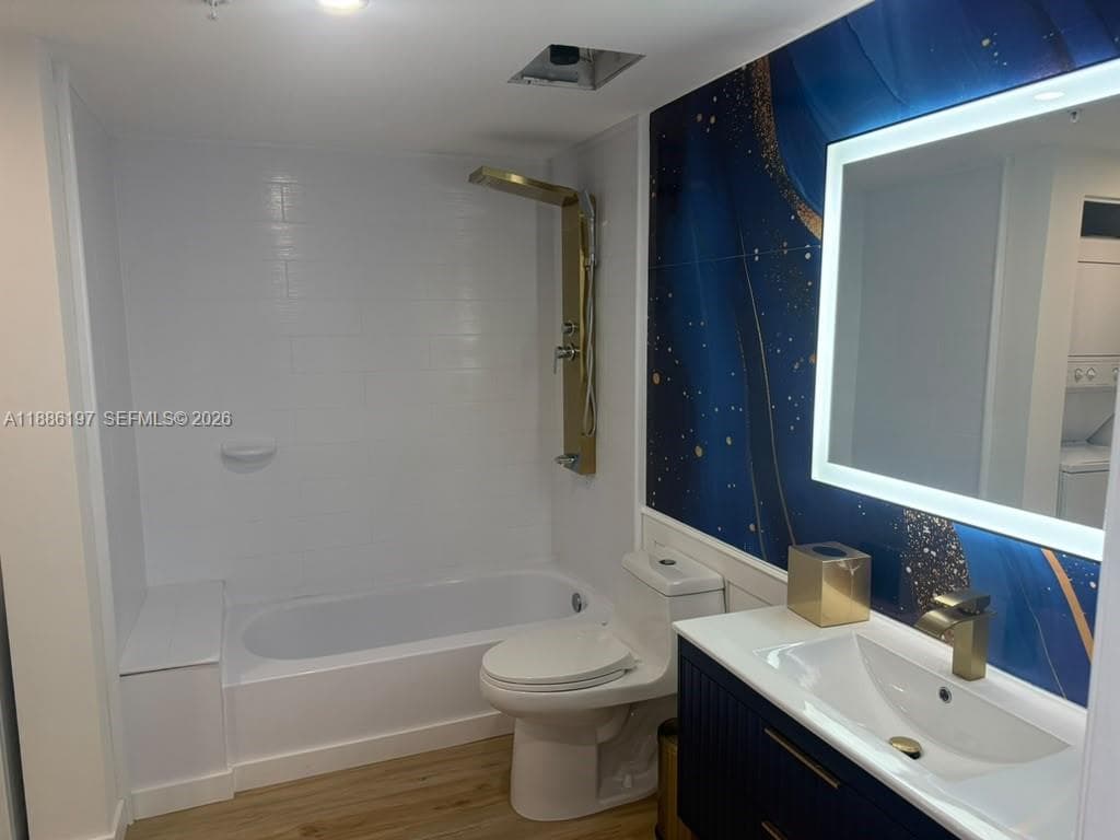 Bathroom featuring a vanity with gold-tone hardware, an LED-backlit mirror, wood-finish flooring, and a shower panel system with a built-in tub bench