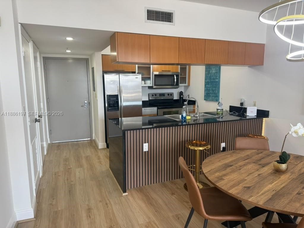 Kitchen featuring wood-finish cabinetry, a peninsula with a slatted base, dark countertops, integrated stainless steel appliances, and wood-finish flooring