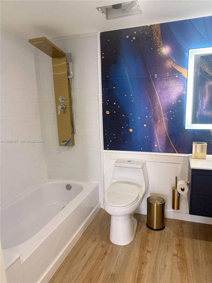 Bathroom featuring a gold-toned shower panel, wood-finish flooring, a wall-mounted lighted mirror, and a decorative blue-and-gold accent wall