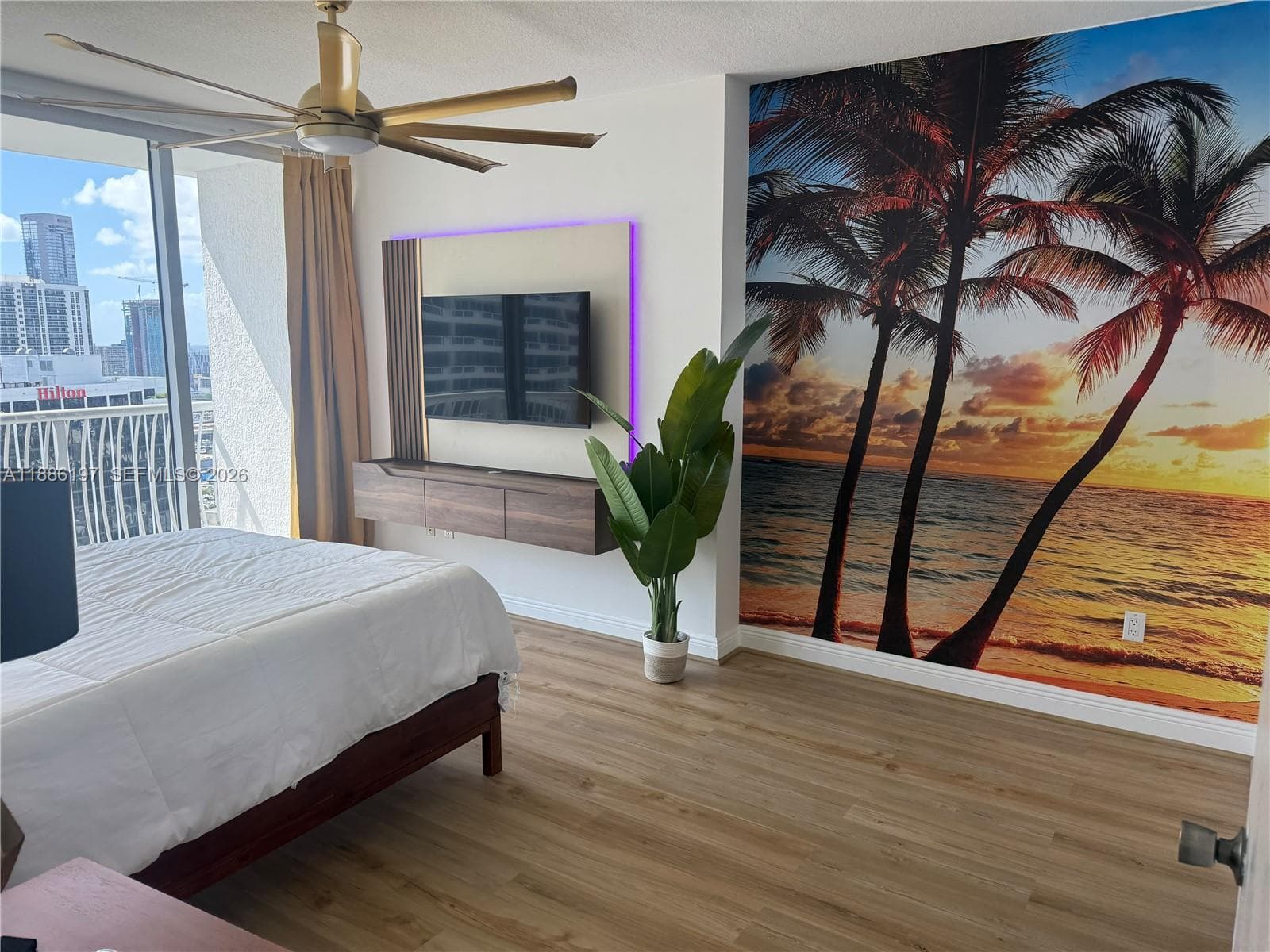 Wood-finish flooring, floating media console with backlighting, ceiling fan with metallic finish, and floor-to-ceiling glass sliding door