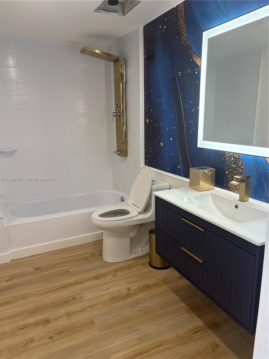 Floating navy blue vanity with gold hardware, integrated LED-backlit mirror, brass shower panel system, wood-finish flooring, and decorative accent wall