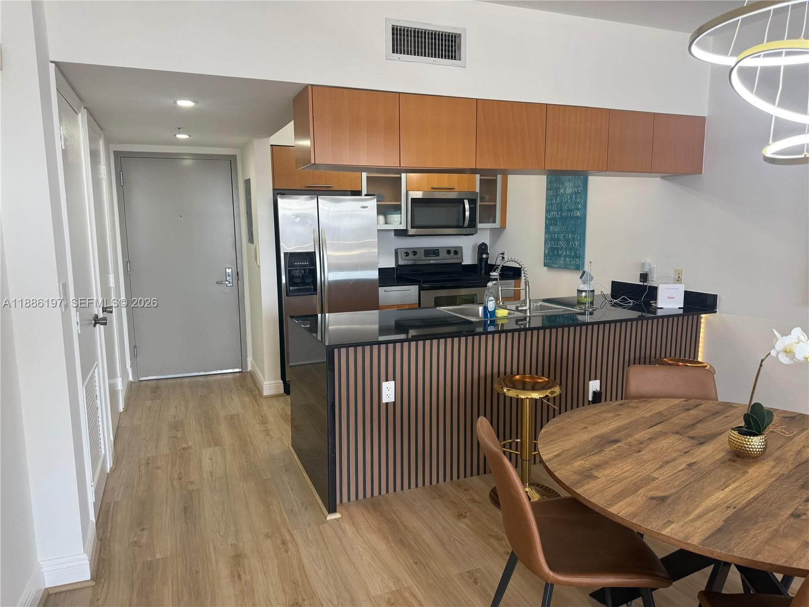 Kitchen featuring stainless steel appliances, dark stone countertops, wood-finish cabinetry, a slatted wood-accented breakfast bar, and wood-finish flooring