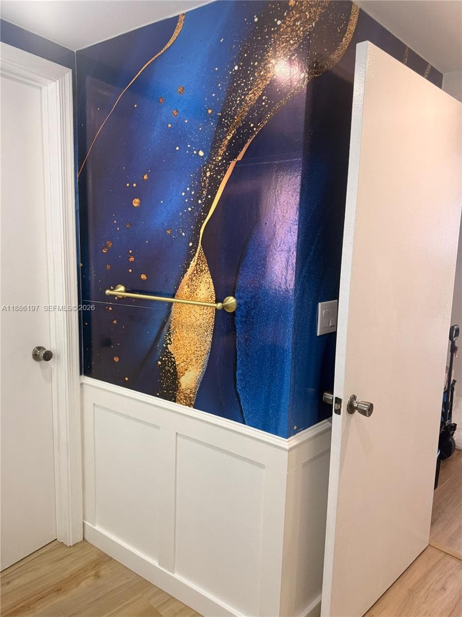 Custom wall covering featuring an abstract deep blue and gold pattern, paired with white wainscoting and a brushed brass towel bar
