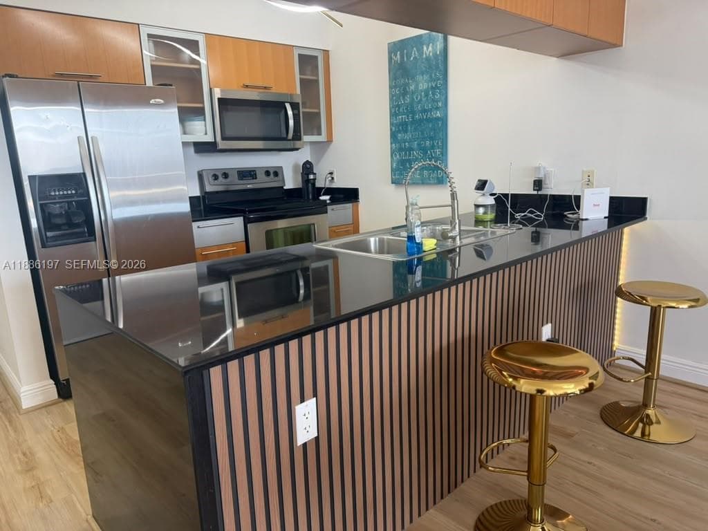 Kitchen featuring wood-finish cabinetry, black stone countertops, stainless steel appliances, and a slatted wood-accented breakfast bar