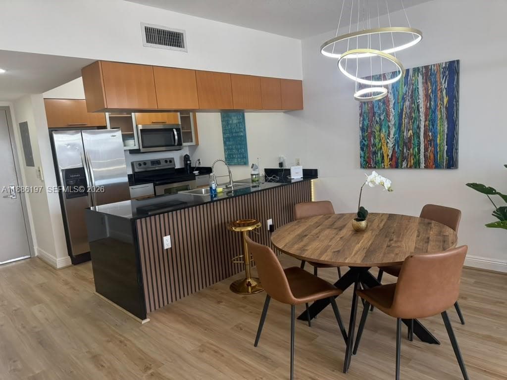 Kitchen featuring a slatted wood-finish peninsula with a dark countertop, stainless steel appliances, flat-panel wood-finish cabinetry, and a contemporary circular tiered chandelier