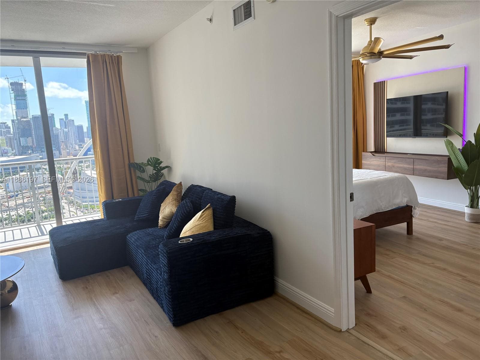 Wood-finish flooring, floor-to-ceiling sliding glass doors, private balcony, built-in floating wooden cabinetry, and overhead ceiling fan