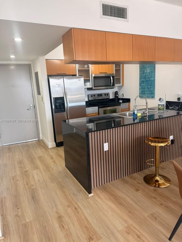 Kitchen featuring an island with a black countertop and vertical wood-slat detailing, wood-finish flooring, stainless steel appliances, and wood cabinetry