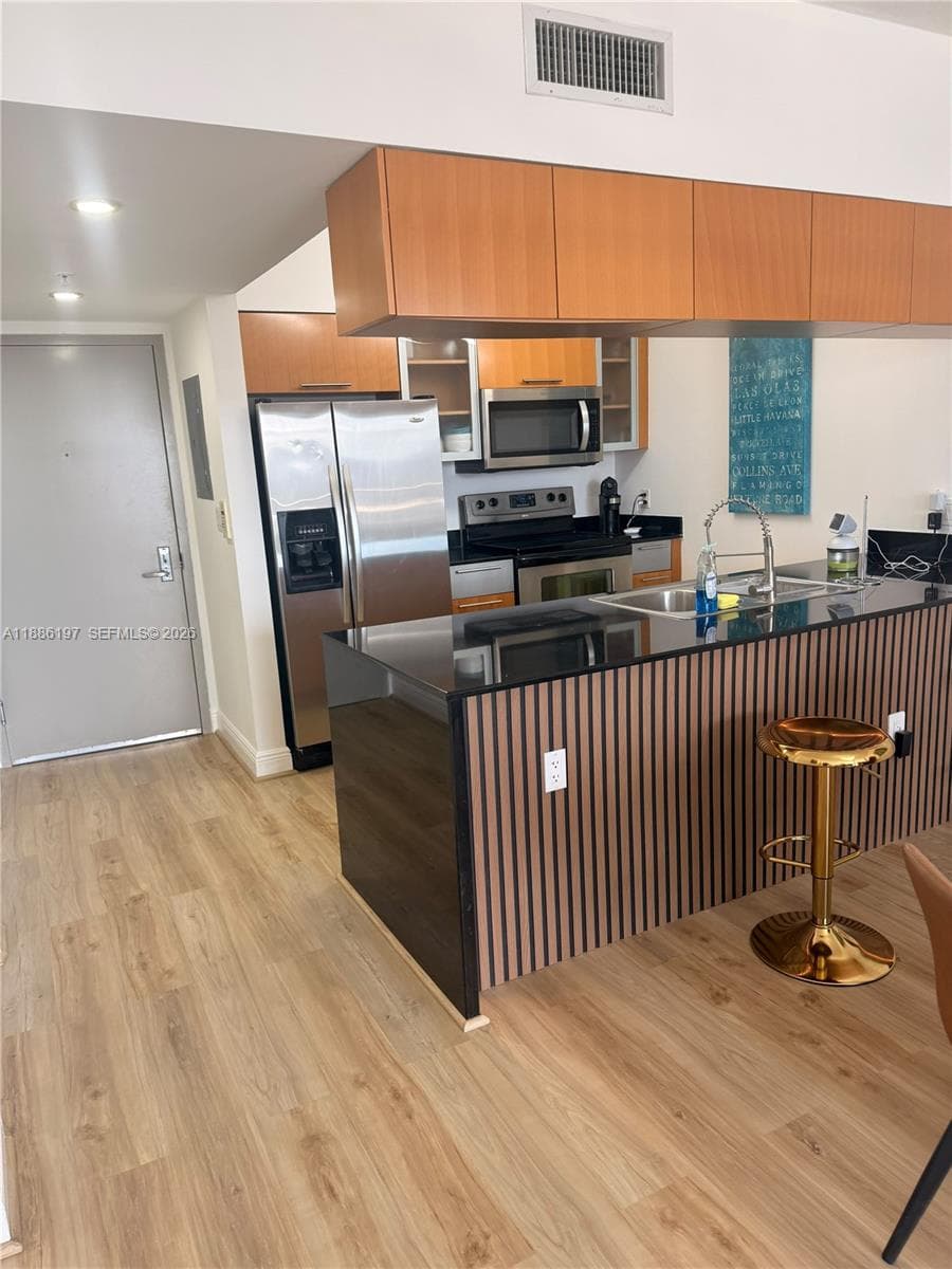 Kitchen featuring wood-finish flooring, cabinetry with horizontal grain, stainless steel appliances, a stone-surfaced island with a vertical-slat facade, and a stainless steel undermount sink