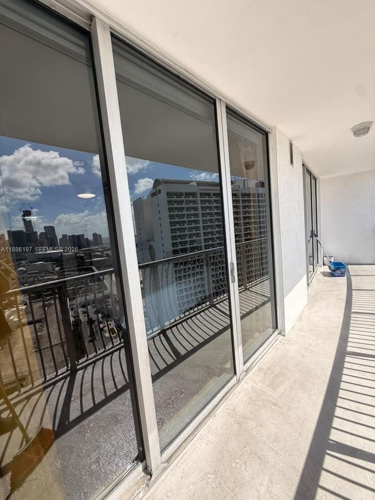 Covered balcony featuring expansive glass sliding doors, metal railings, and concrete flooring