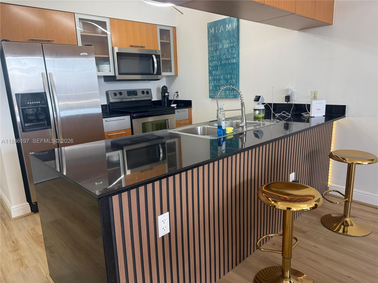 Kitchen featuring wood-toned cabinetry, stainless steel appliances, dark stone-finish countertops, a dual-basin sink with a gooseneck faucet, and an island accented with vertical wood-slat paneling