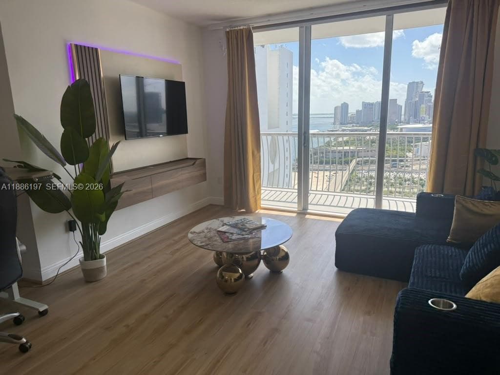 Living area featuring wood-finish flooring, floor-to-ceiling glass sliding doors, a wall-mounted floating wood-finish media console, and an accent wall with integrated ambient lighting