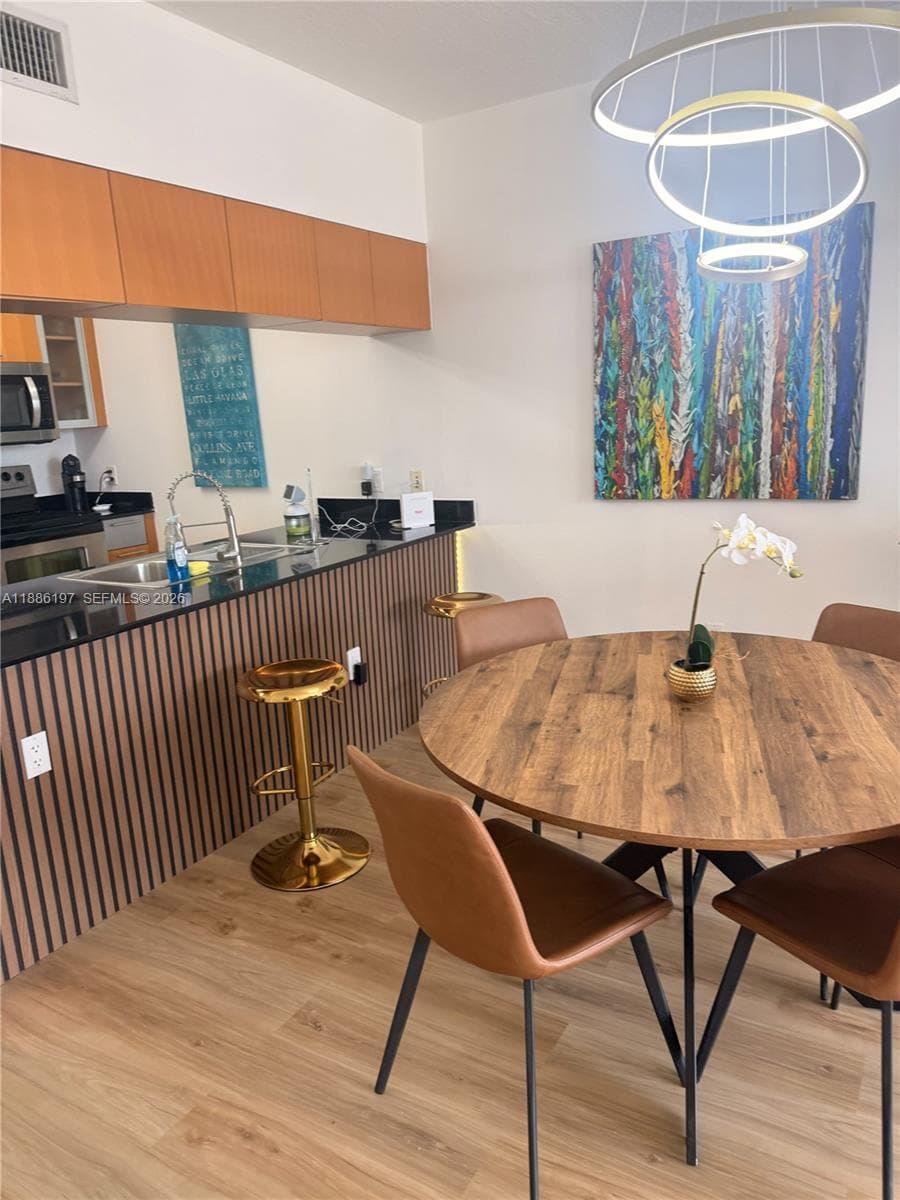 Kitchen featuring a wood-slat breakfast bar with a black stone countertop, flat-panel cabinetry, wood-finish flooring, and a modern circular tiered chandelier