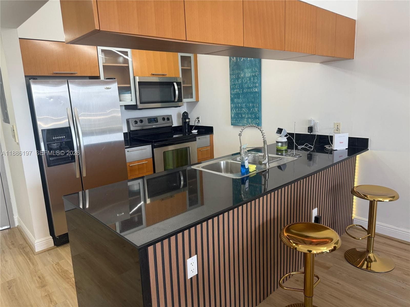 Kitchen featuring a peninsula with a dark stone countertop, wood-slat paneling, integrated stainless steel appliances, flat-panel wood cabinetry, and wood-finish flooring