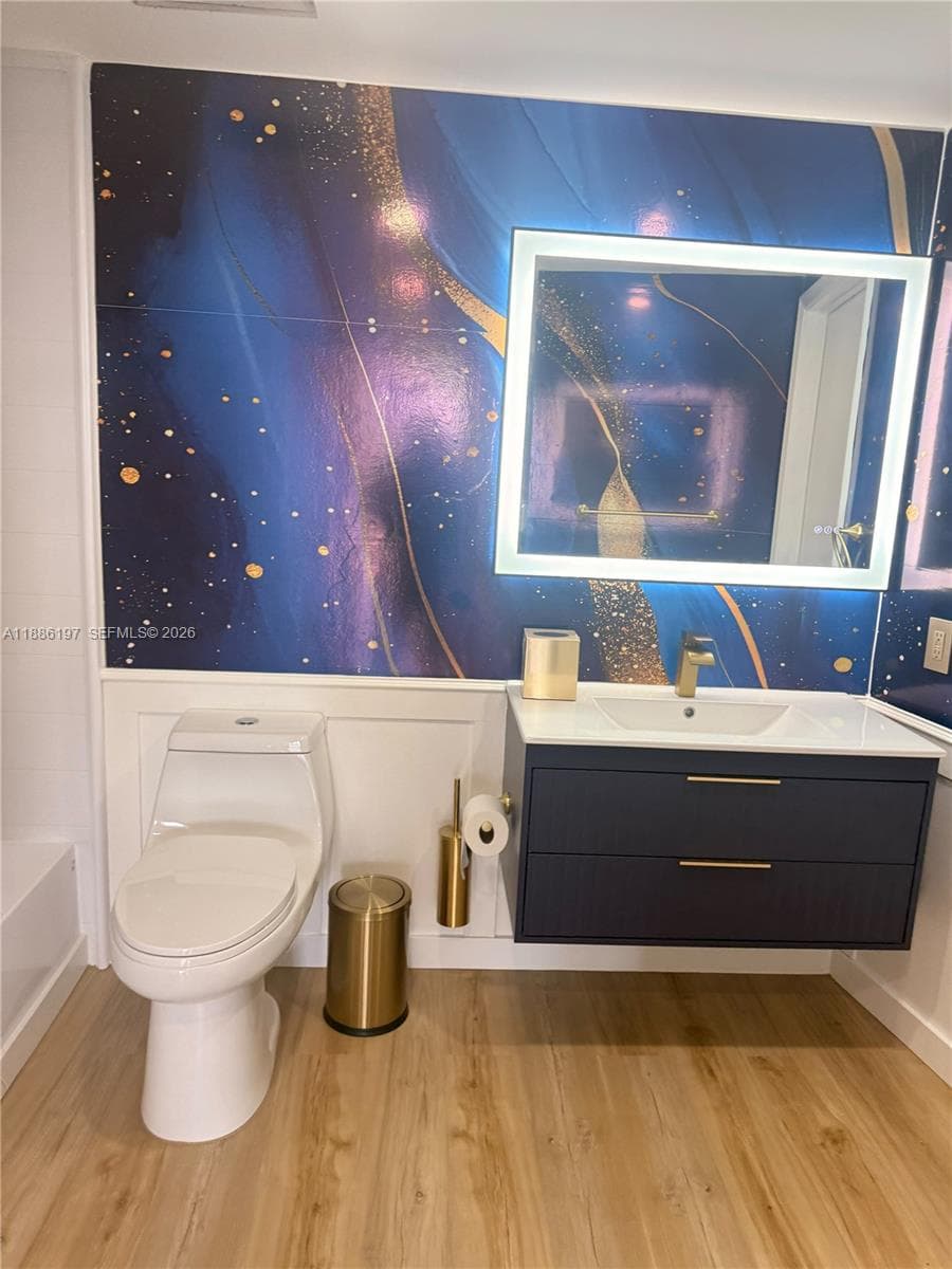 Floating vanity with two drawers, integrated rectangular sink, wall-to-wall patterned decorative wall paneling, white wainscoting, and rectangular LED-backlit mirror
