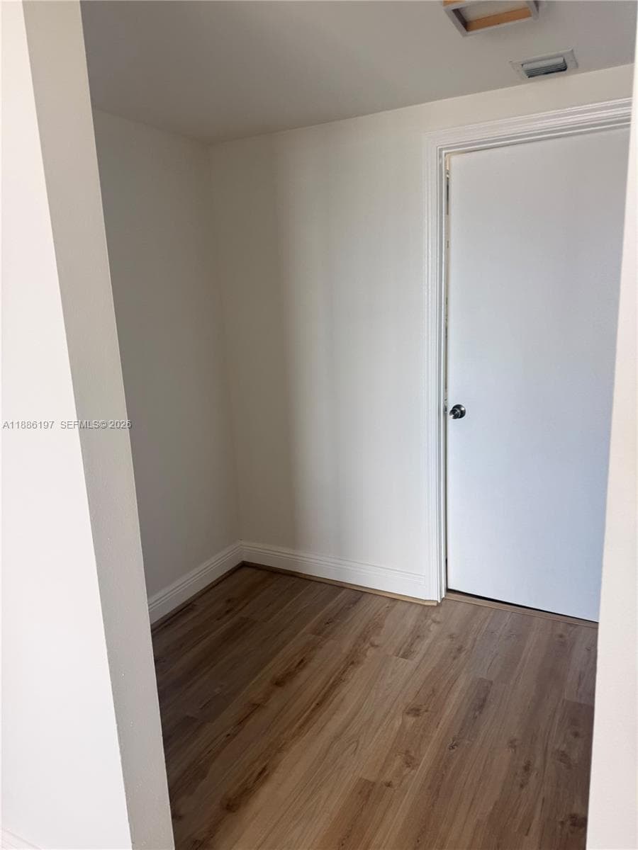 Neutral interior space featuring wood-finish flooring, a solid core interior door with a circular knob, and recessed ceiling lighting