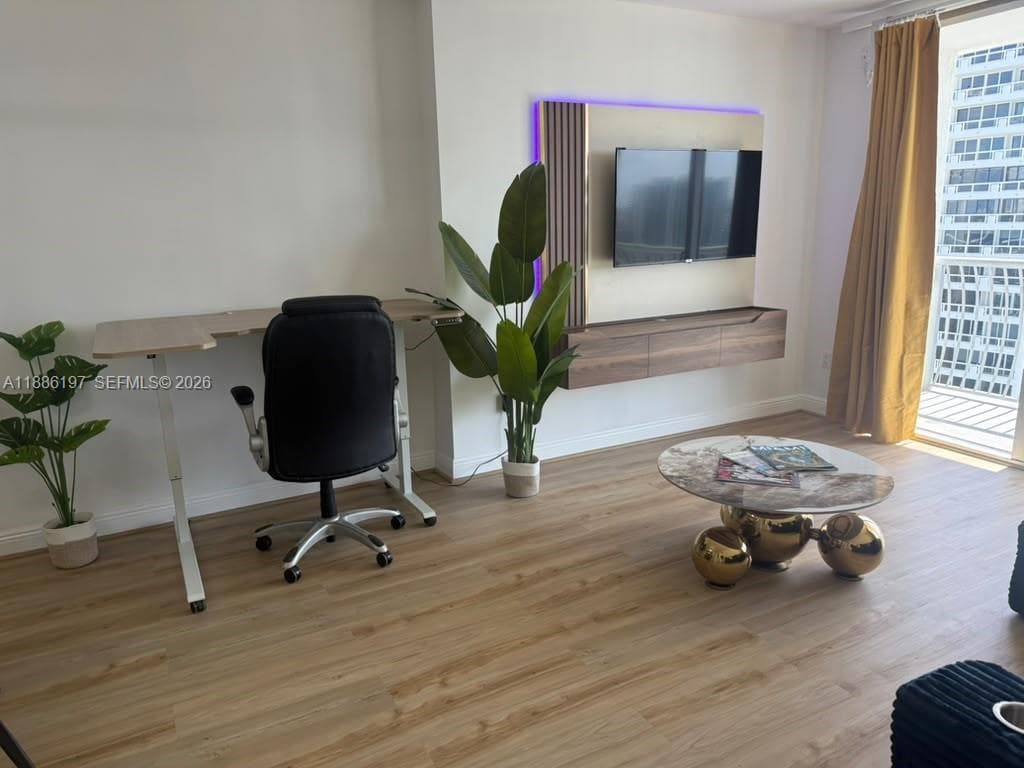 Wood-finish flooring, wall-mounted media console with integrated vertical paneling, and access to a private balcony