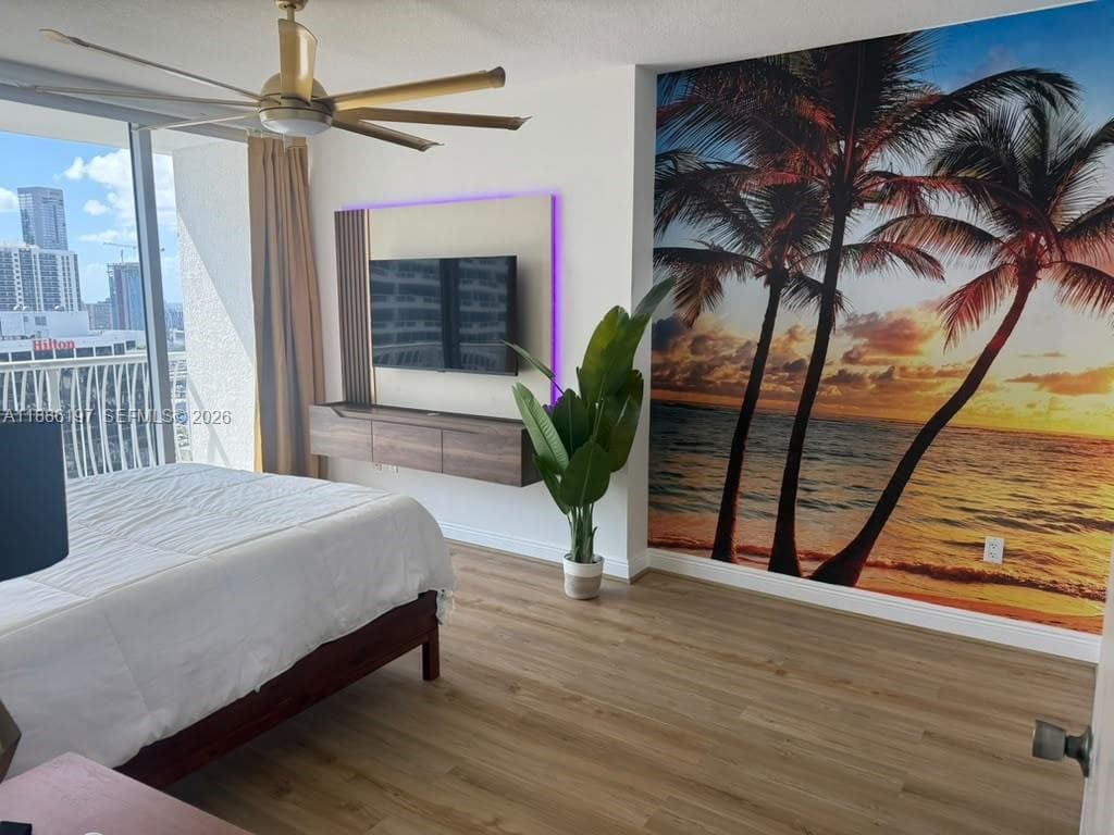 Floor-to-ceiling glass sliding doors, wood-finish flooring, floating media console with integrated accent lighting, and a multi-blade ceiling fan