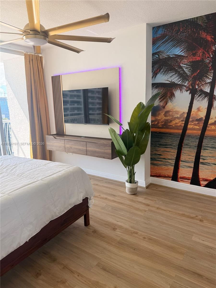 Wood-finish flooring, ceiling fan with metallic blades, and a wall-mounted floating media console featuring integrated backlighting