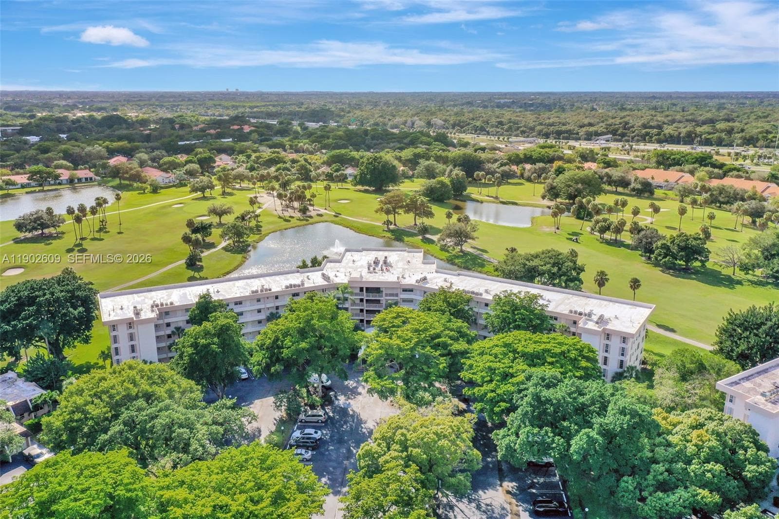 Aerial view of the lush golf course and lake — wide fairways, tranquil water features, and palm-dotted greens wrap the community in resort-style scenery.