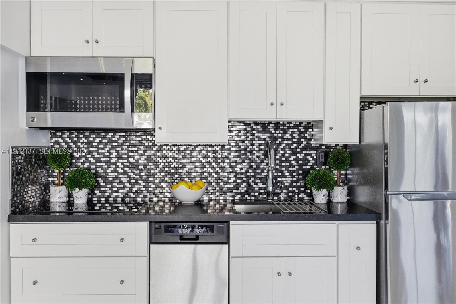 This stylish kitchen combines contemporary design with everyday functionality. Featuring crisp white cabinetry, elegant black stone countertops, and a striking mosaic tile backsplash, the space exudes modern sophistication. The high-end induction cooktop offers precise temperature control and energy efficiency, complemented by stainless-steel appliances and a deep chrome sink. Beautifully updated culinary space — perfect for both cooking and entertaining.