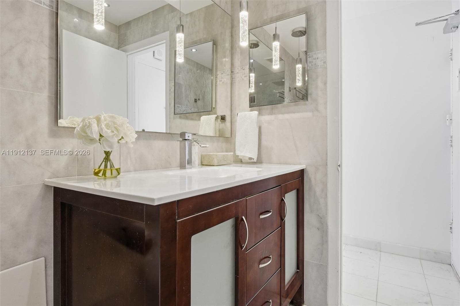 Spacious spa-inspired bathroom, beautifully finished in floor-to-ceiling marble. The frameless glass shower features a rainfall showerhead and built-in bench, creating a relaxing retreat. A rich wood vanity with sleek chrome fixtures and underlit modern lighting adds warmth and sophistication, while the large mirror enhances the sense of space and light. Every detail has been thoughtfully designed to offer a serene, hotel-quality experience in the comfort of home