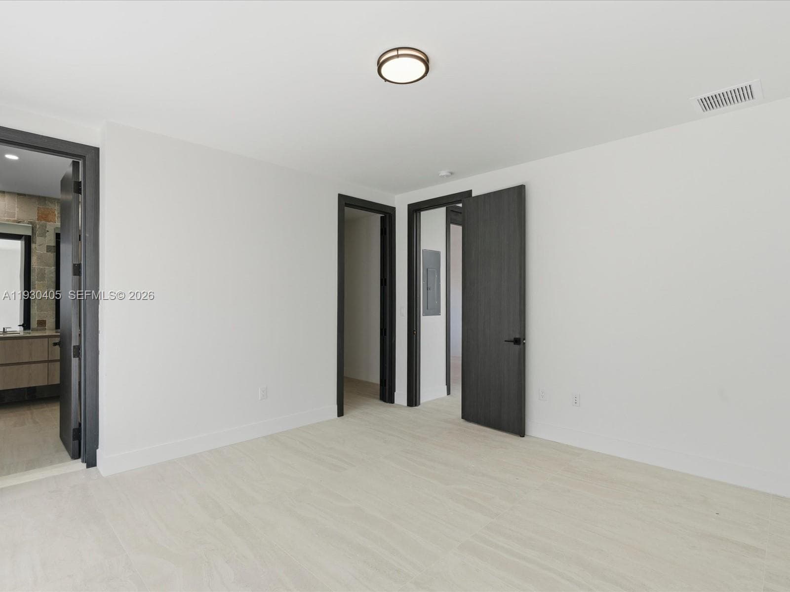 Neutral-toned stone-finish flooring, dark-stained interior doors, matte black door hardware, and a minimalist flush-mount ceiling fixture