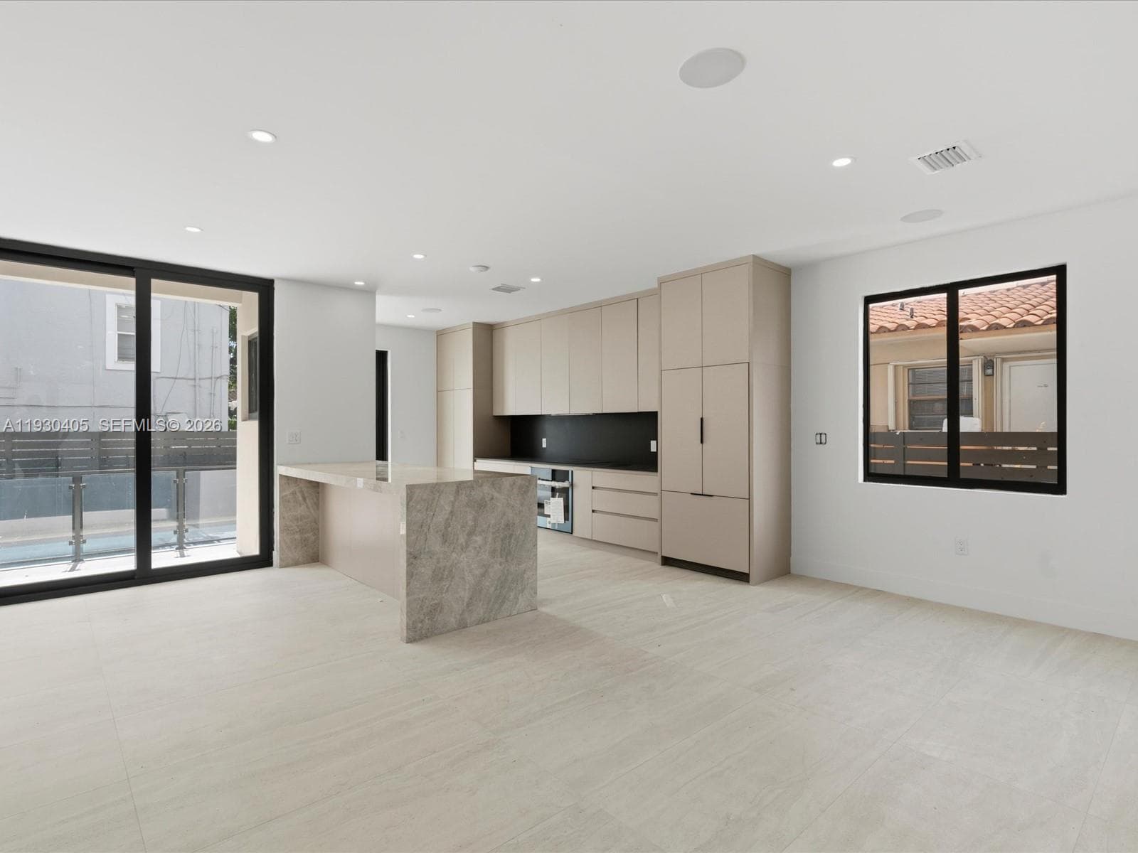 Kitchen featuring floor-to-ceiling cabinetry, a stone-finish waterfall island, matte black backsplash, integrated refrigerator, and large-format tile flooring