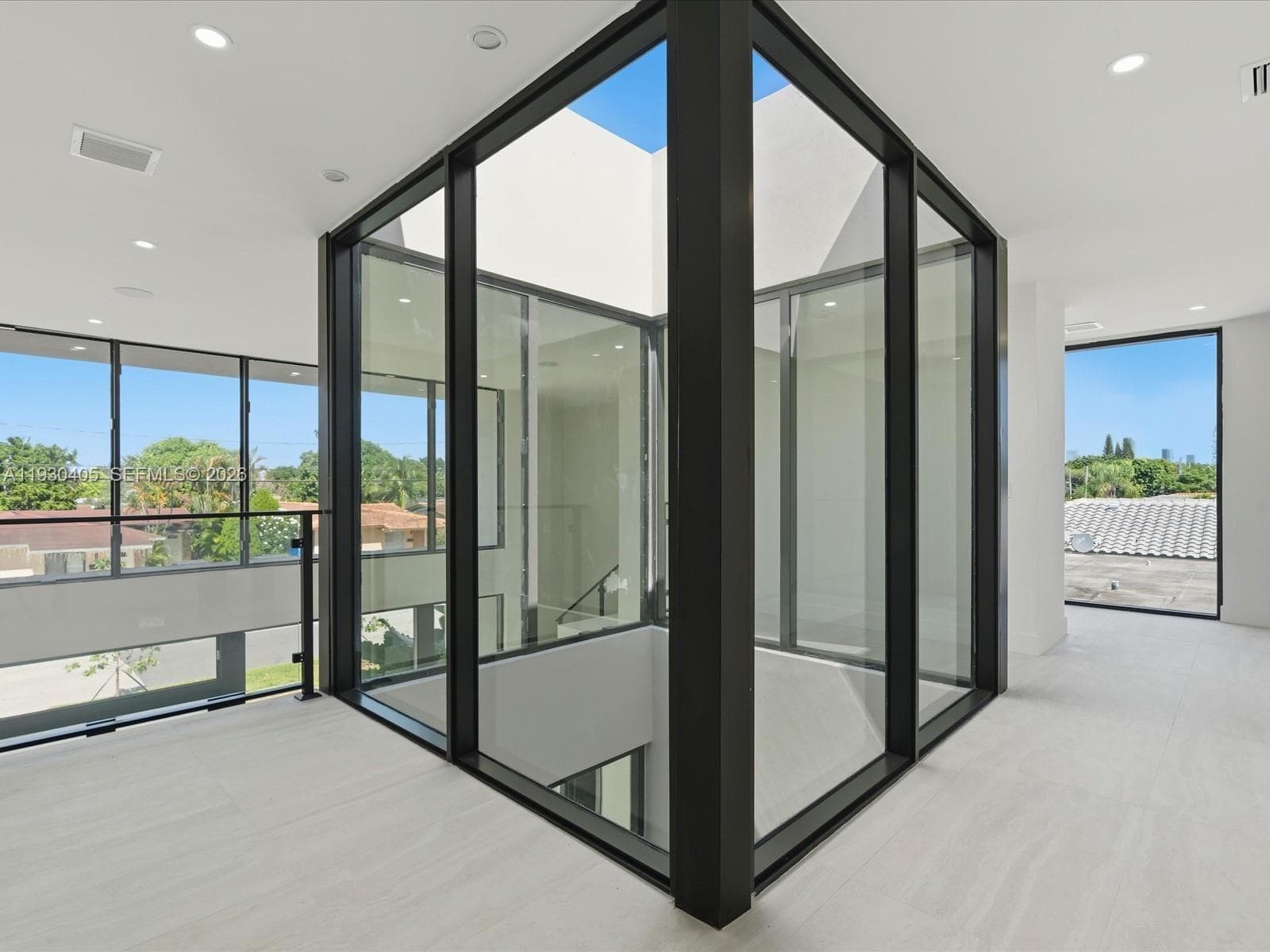 Central glass-encased atrium featuring floor-to-ceiling windows and metal framing, complemented by recessed lighting and neutral stone-finish flooring