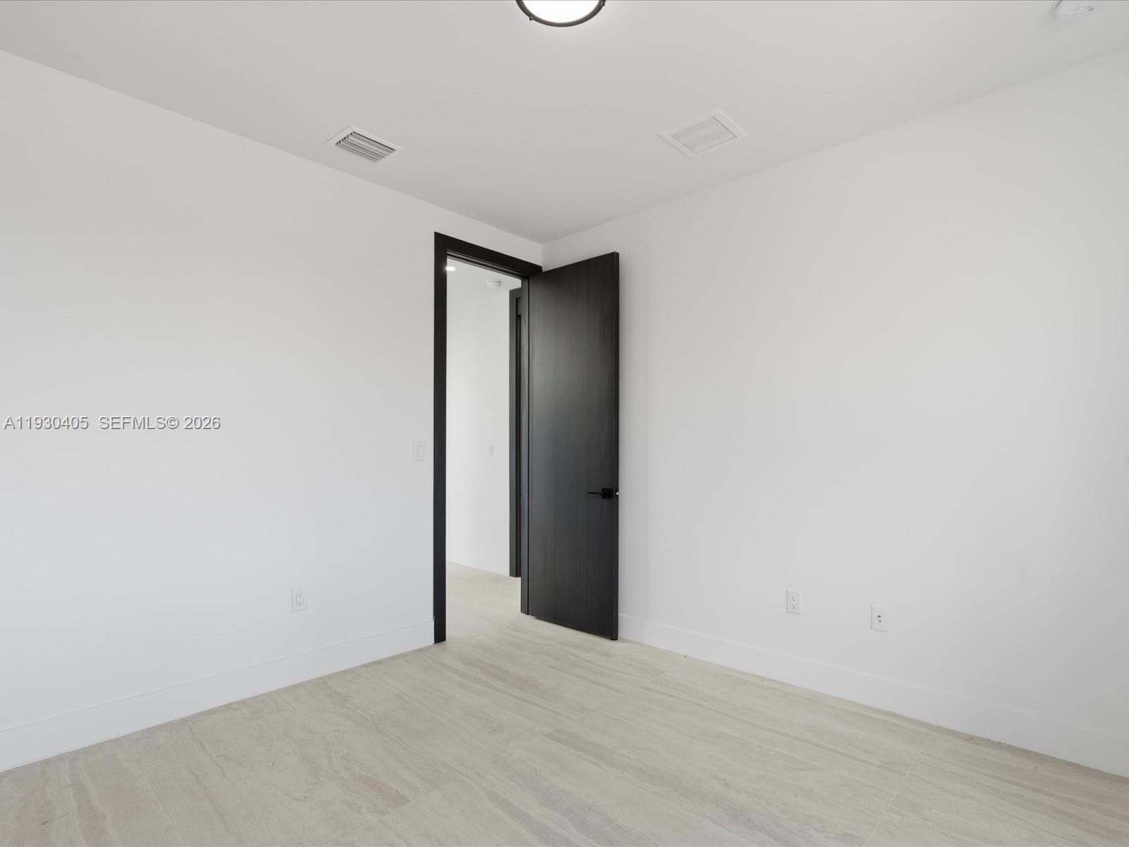 Interior space featuring light-toned wood-finish flooring, a matte black door with matching hardware, and a neutral white color palette