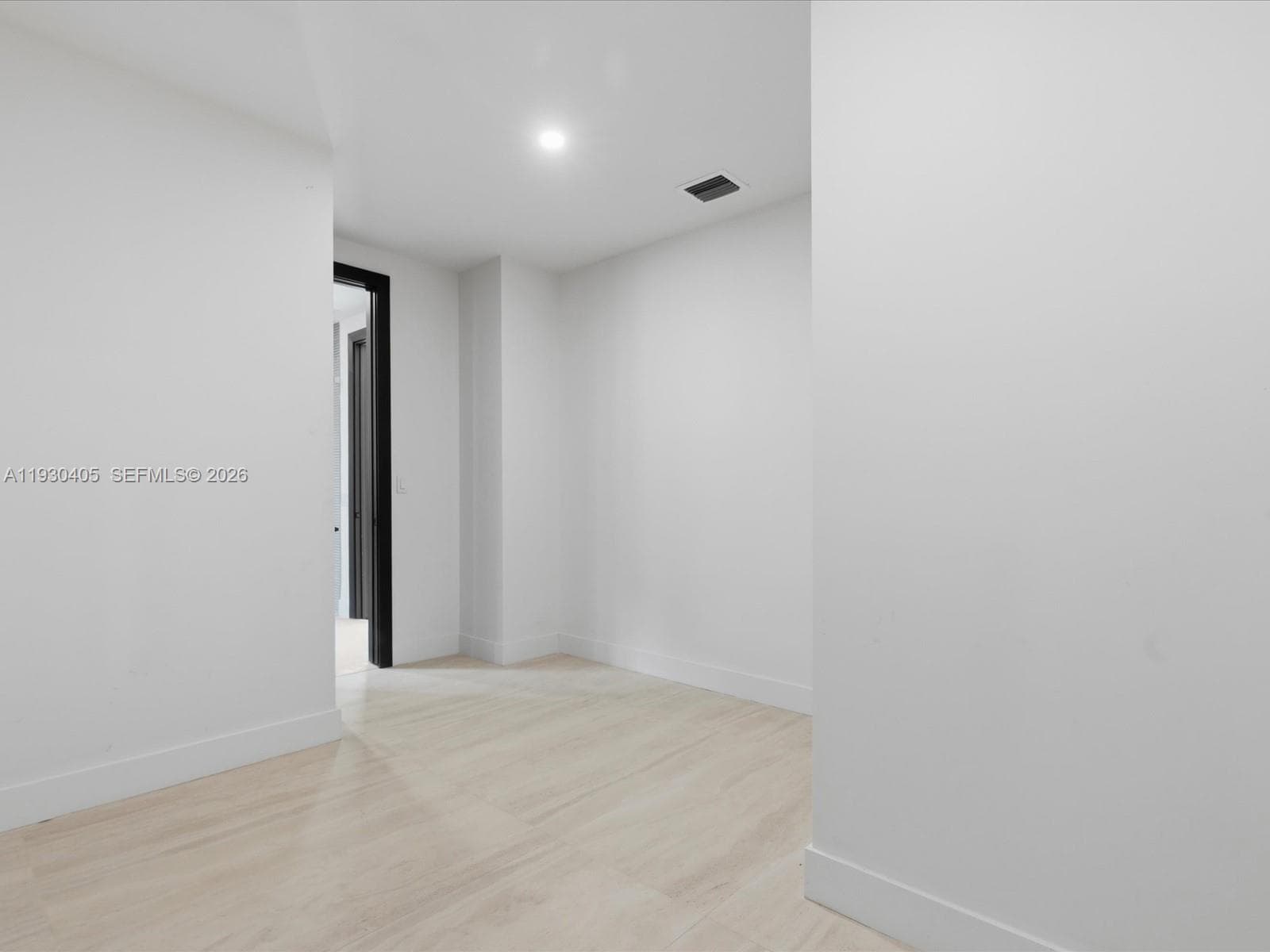 Interior space featuring light-toned wood-finish flooring, crisp white walls, recessed ceiling lighting, and a dark-framed doorway