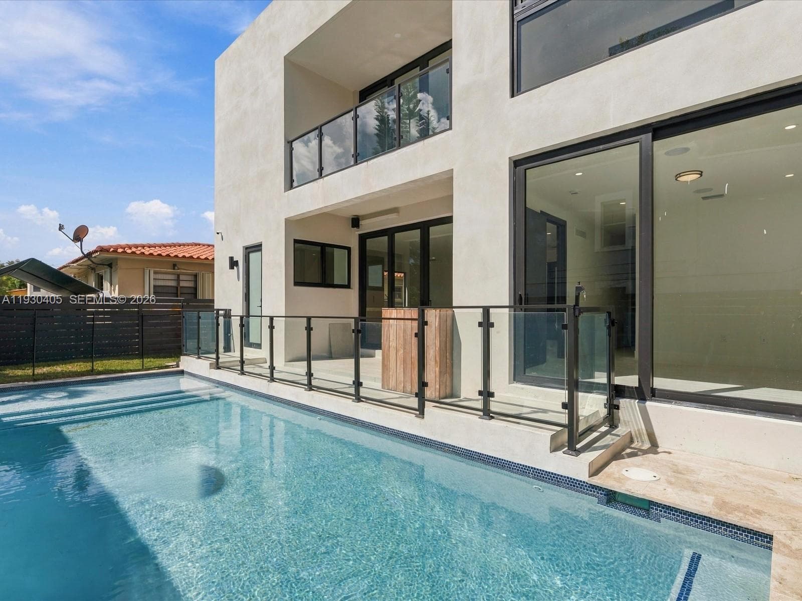 Contemporary two-story exterior featuring smooth stucco siding, large-format sliding glass doors, a second-story balcony with glass railings, and a recessed swimming pool with stone decking