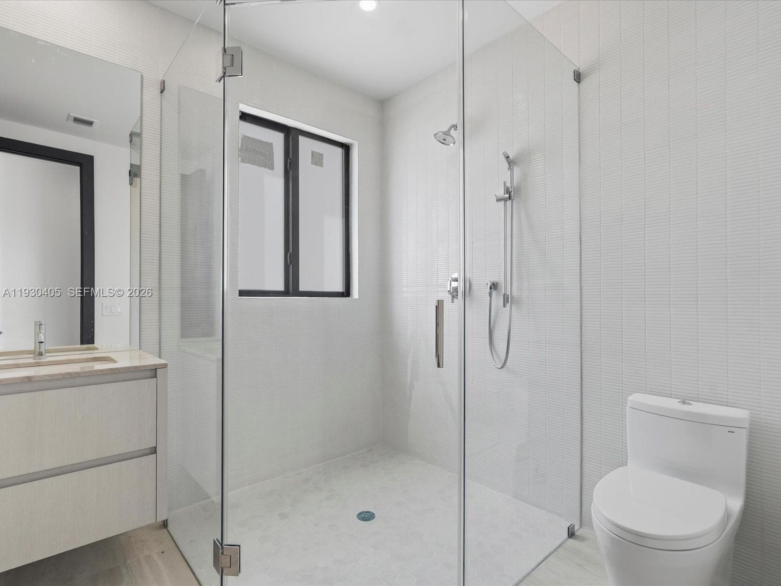 Walk-in shower with a glass enclosure, wall-mounted showerhead, hand-held sprayer, and stacked tile surround