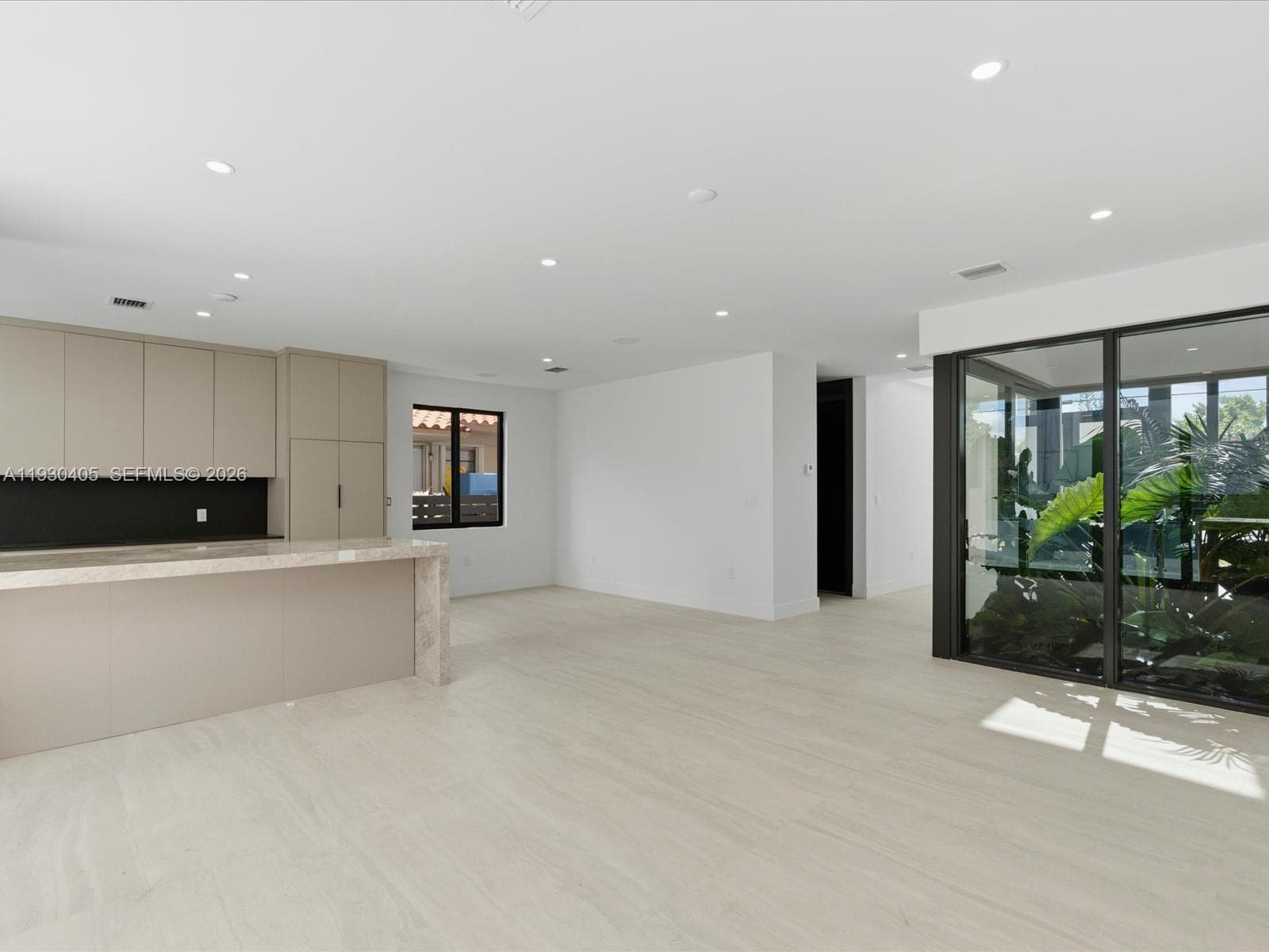 Open-concept area featuring neutral oversized tile flooring, recessed ceiling lighting, kitchen cabinetry with stone-surface counters, and large-format sliding glass doors