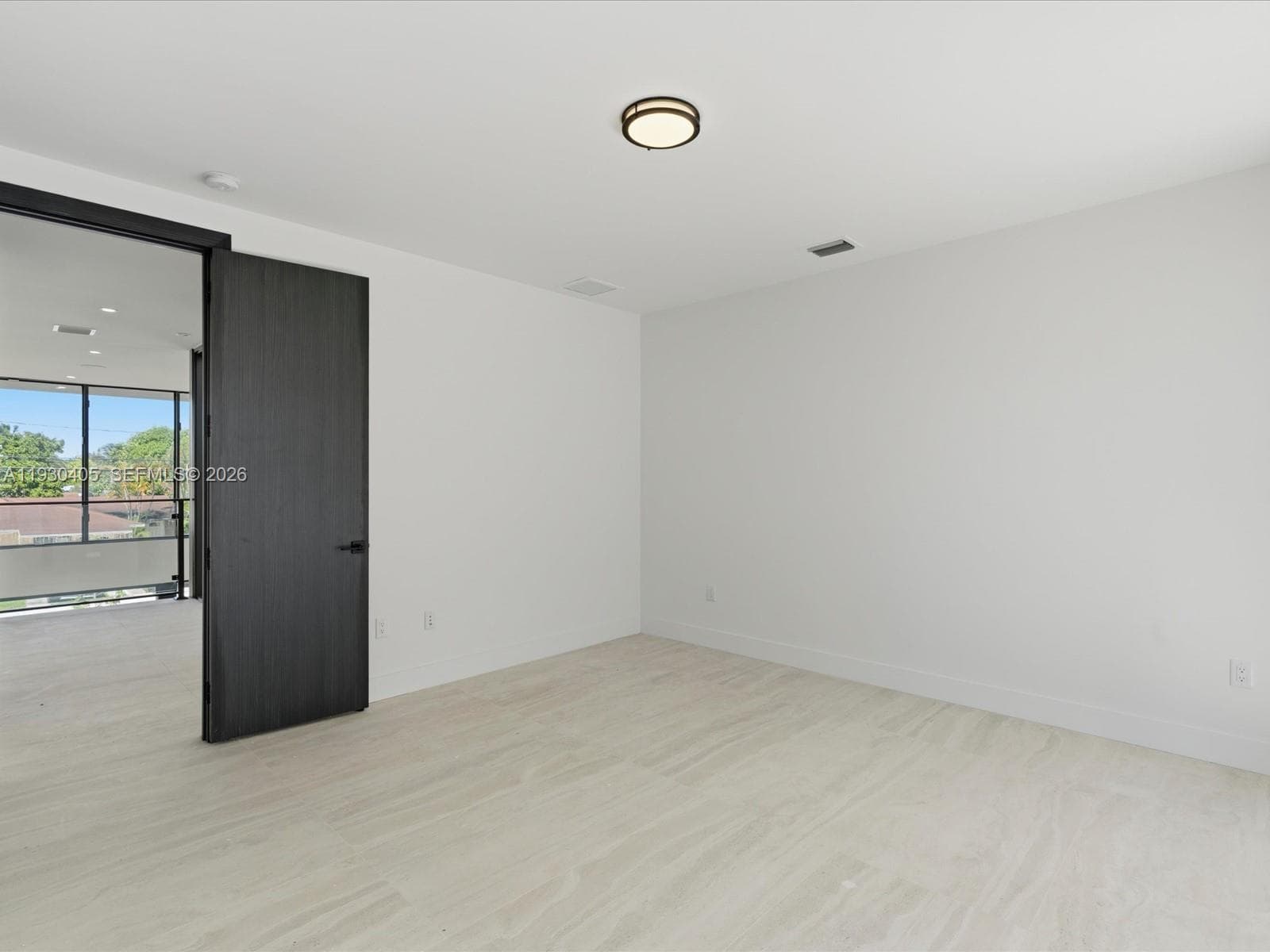 Neutral-toned stone flooring, dark-stained wood door with matte black hardware, and a modern circular ceiling-mounted light fixture