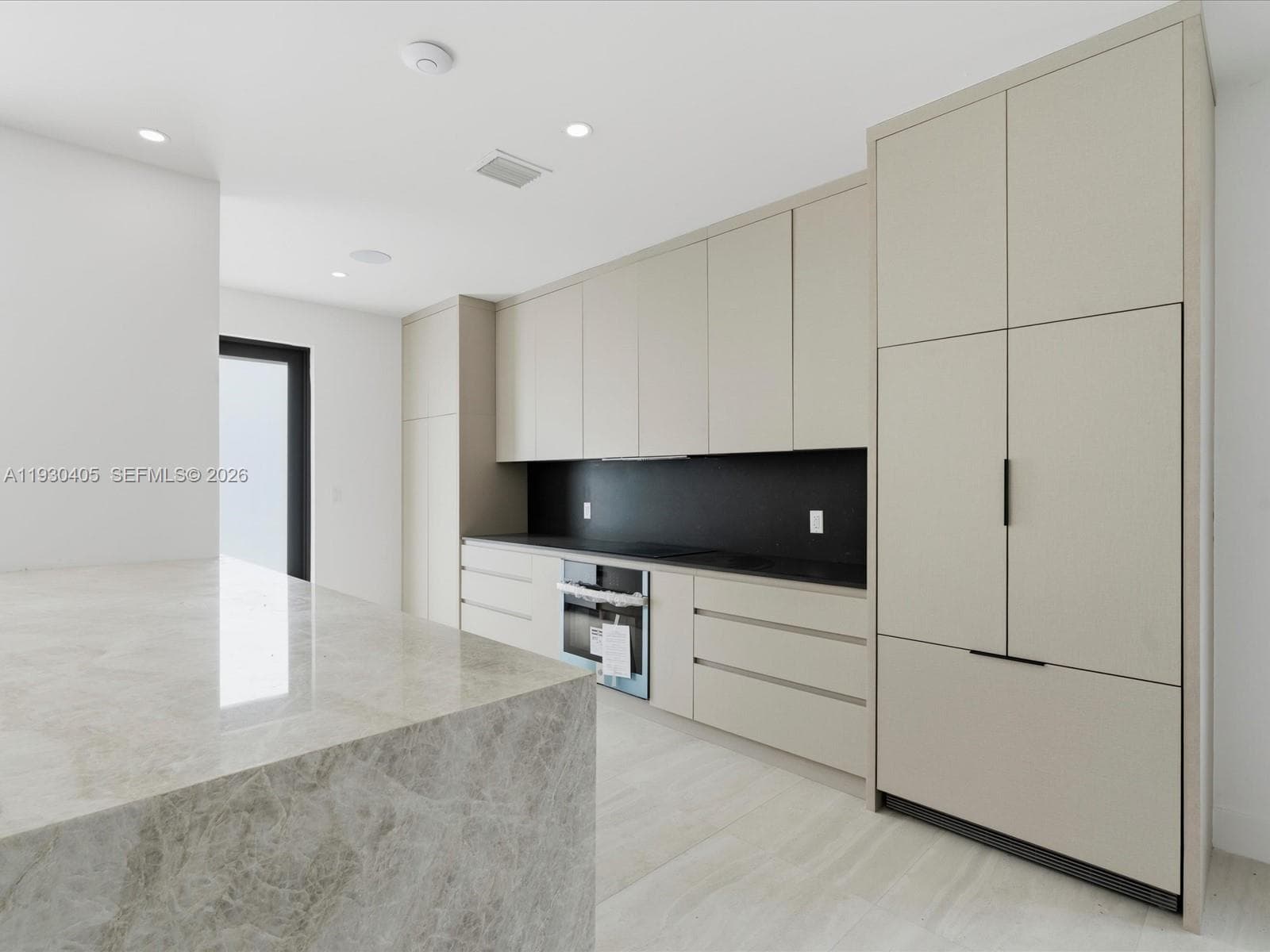 Kitchen featuring floor-to-ceiling cabinetry, a stone-top waterfall island, contrasting black backsplash, integrated appliances, and recessed lighting