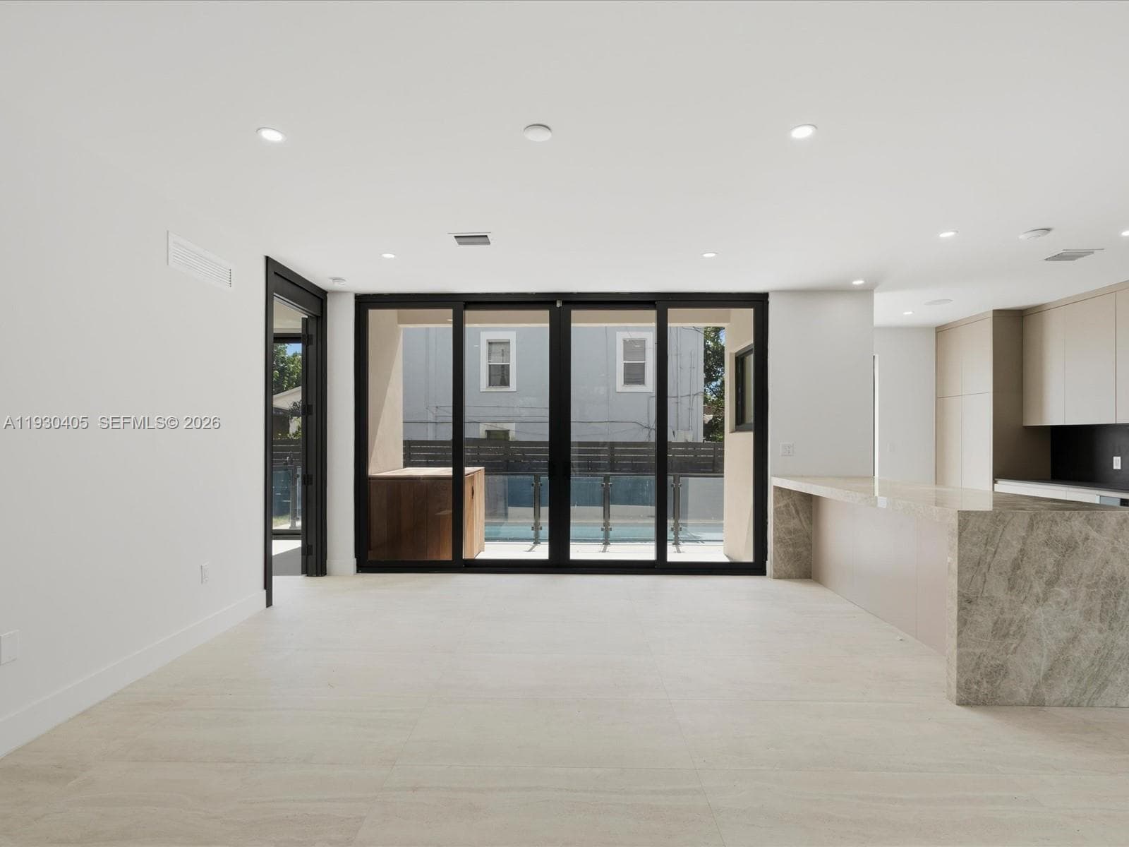 Open-concept interior featuring large-format stone tile flooring, a stone-top kitchen island with waterfall edge, flat-panel cabinetry, and multi-panel sliding glass doors