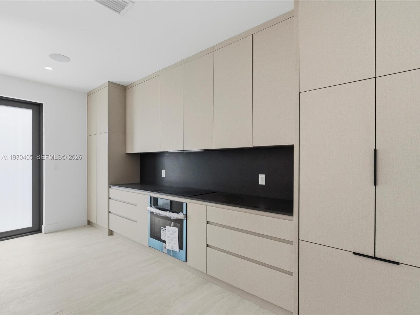 Kitchen featuring minimalist floor-to-ceiling cabinetry, matte black hardware, solid-surface countertops, contrast backsplash, and integrated oven