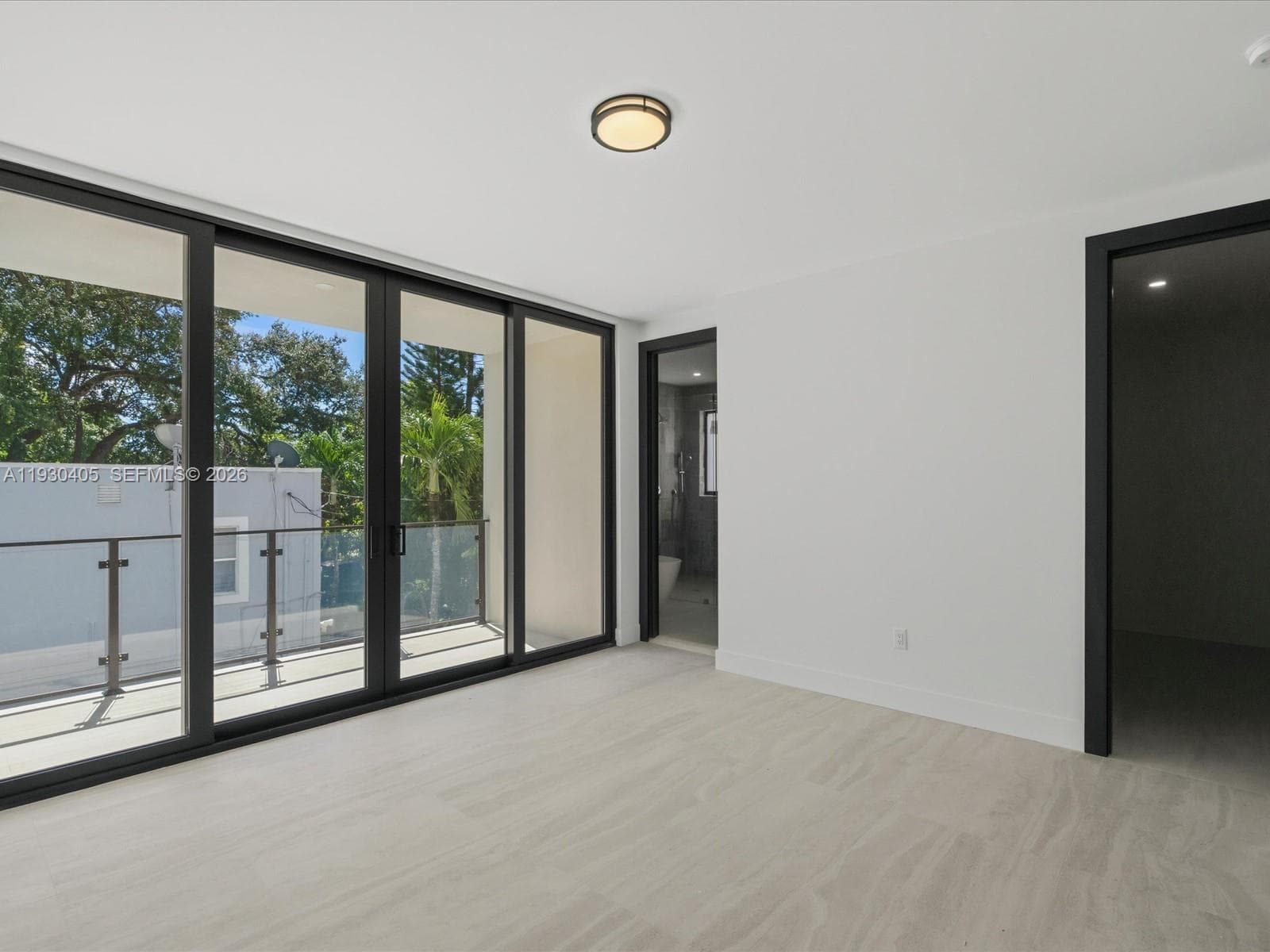 Floor-to-ceiling sliding glass doors, neutral stone-finish flooring, private balcony with glass railing, and dark-finish door frames