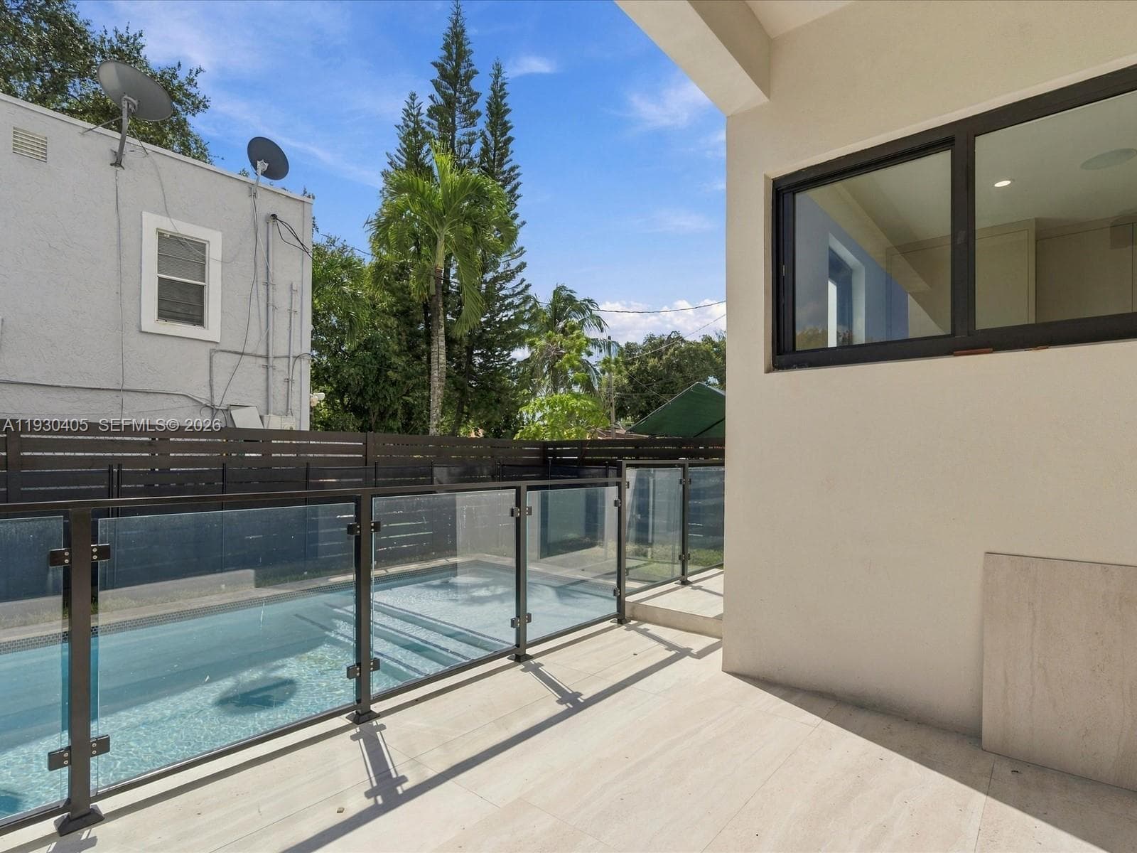 Covered patio with large-format tile flooring, swimming pool, glass railing system, and horizontal wood-slat privacy fencing