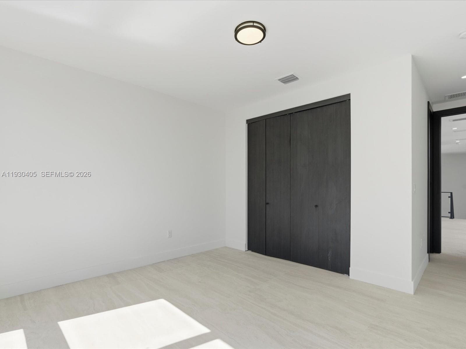 Interior space featuring wood-finish flooring, charcoal-toned bi-fold closet doors, and a central circular ceiling-mounted light fixture