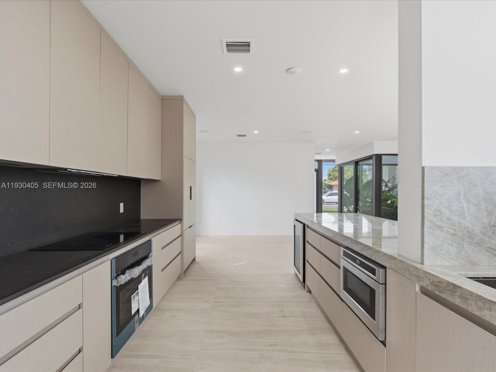 Modern kitchen featuring light-toned slab cabinetry, solid-surface countertops, recessed ceiling lighting, and built-in stainless steel appliances