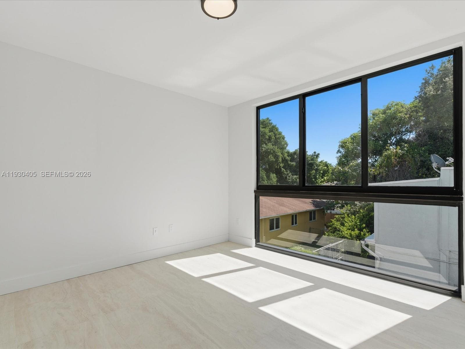 Expansive floor-to-ceiling windows with black frames, light-toned wood-finish flooring, and minimalist white walls