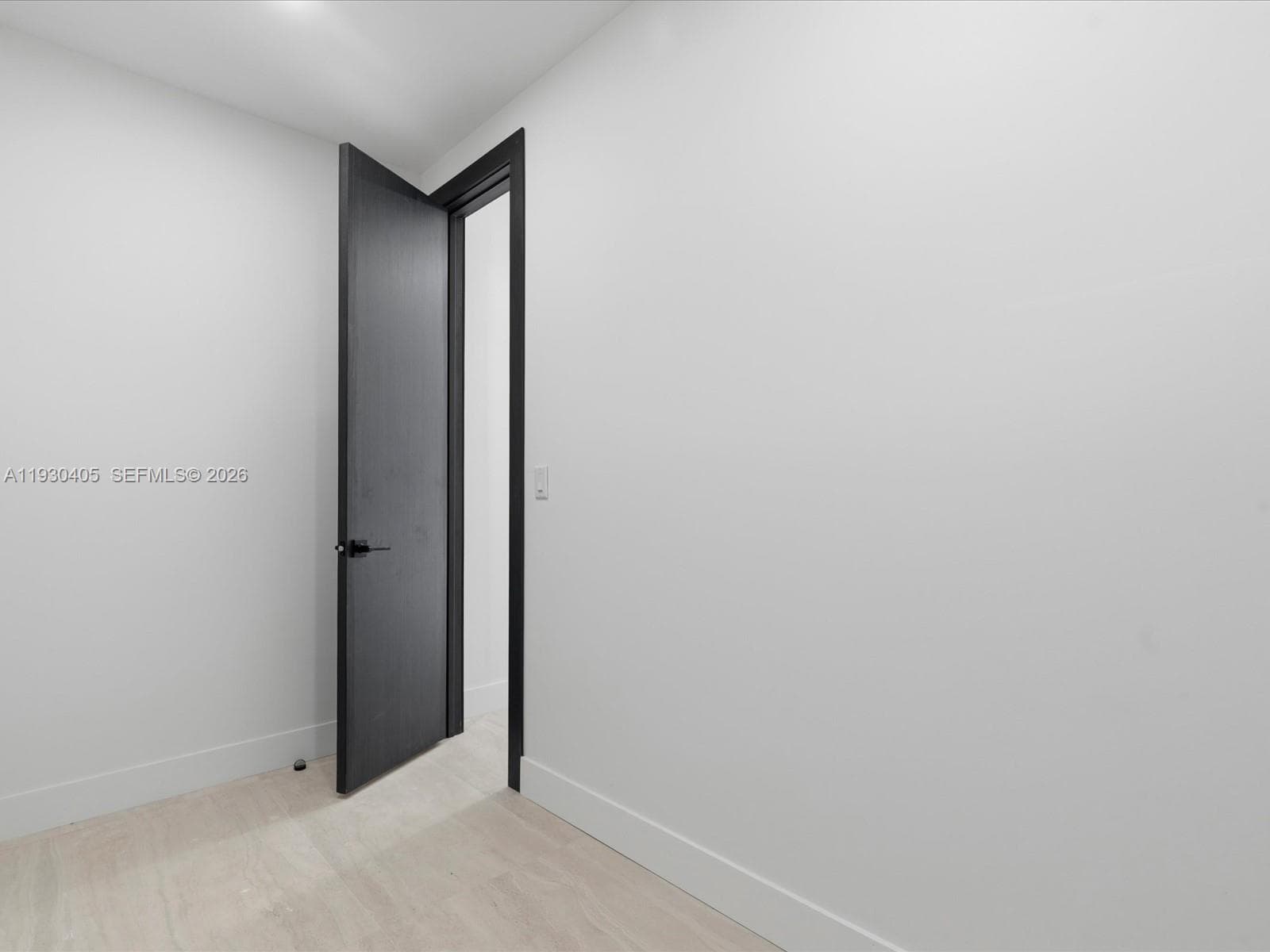 Neutral-toned walls, light-finished flooring, and a solid-core interior door featuring a matte black lever handle and matching door casing