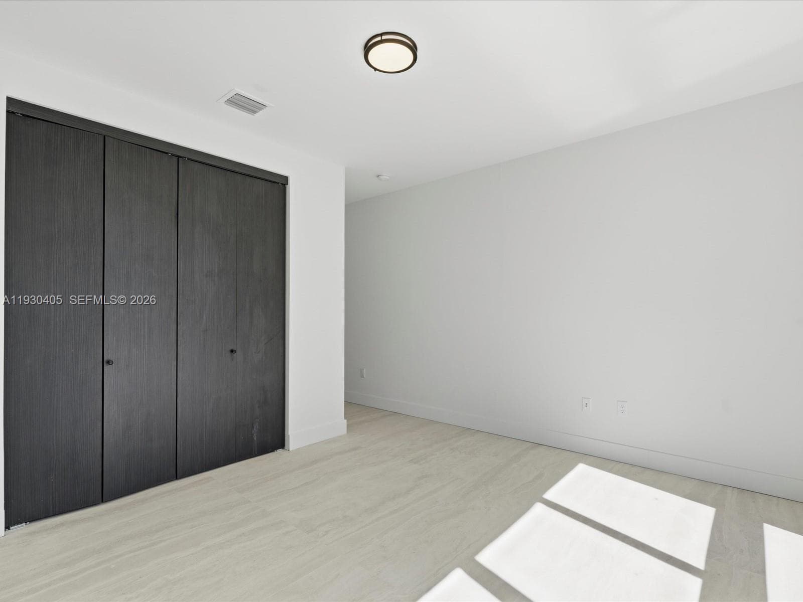 Interior space featuring light-toned wood-finish flooring, charcoal-toned floor-to-ceiling closet doors with knob hardware, and a circular flush-mount ceiling light fixture
