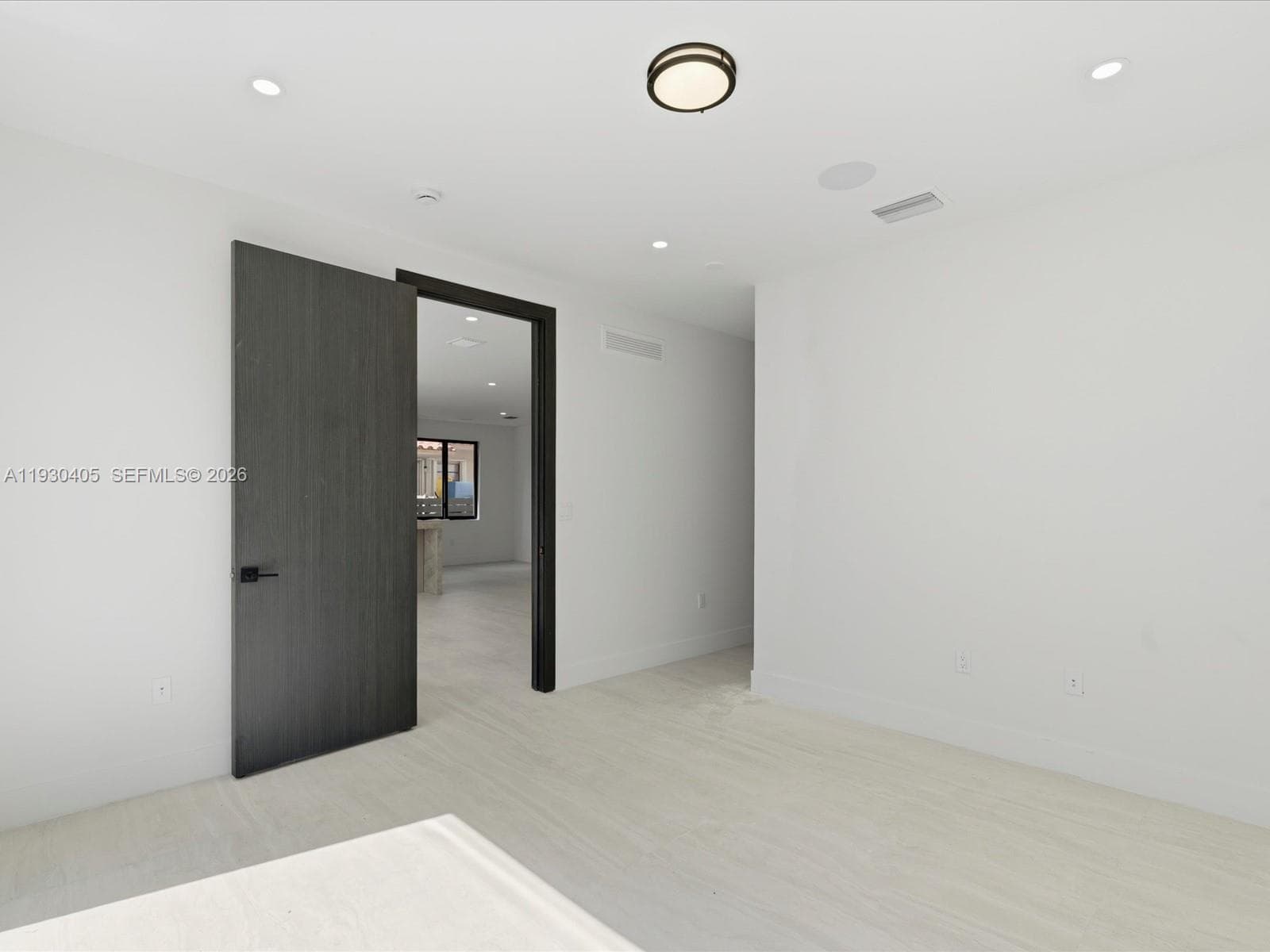 Interior space featuring light wood-finish flooring, charcoal-toned door with matte black hardware, recessed ceiling lighting, and a circular flush-mount fixture
