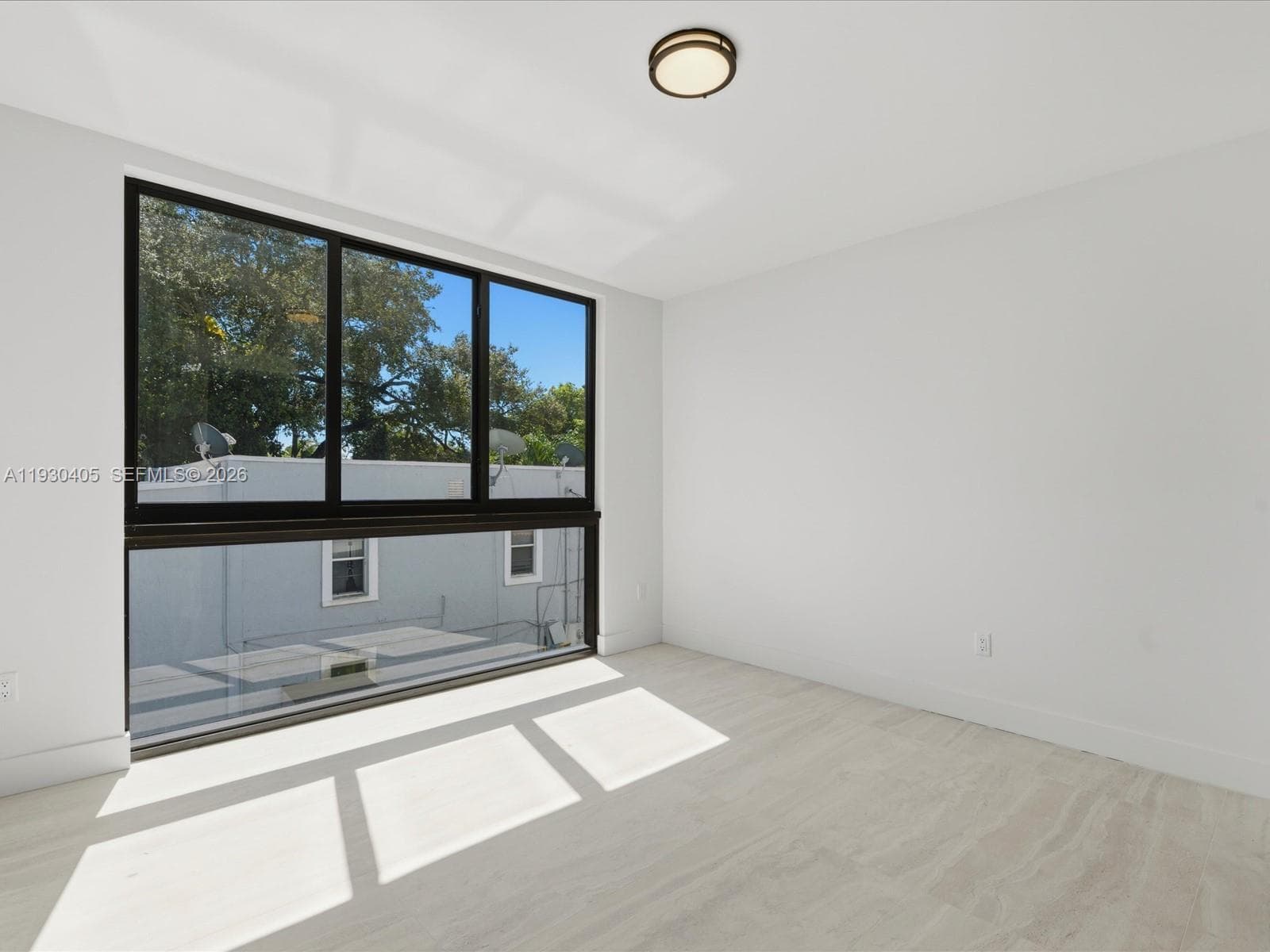 Large multi-panel window with black framing, wood-finish flooring, and flush-mount circular ceiling lighting