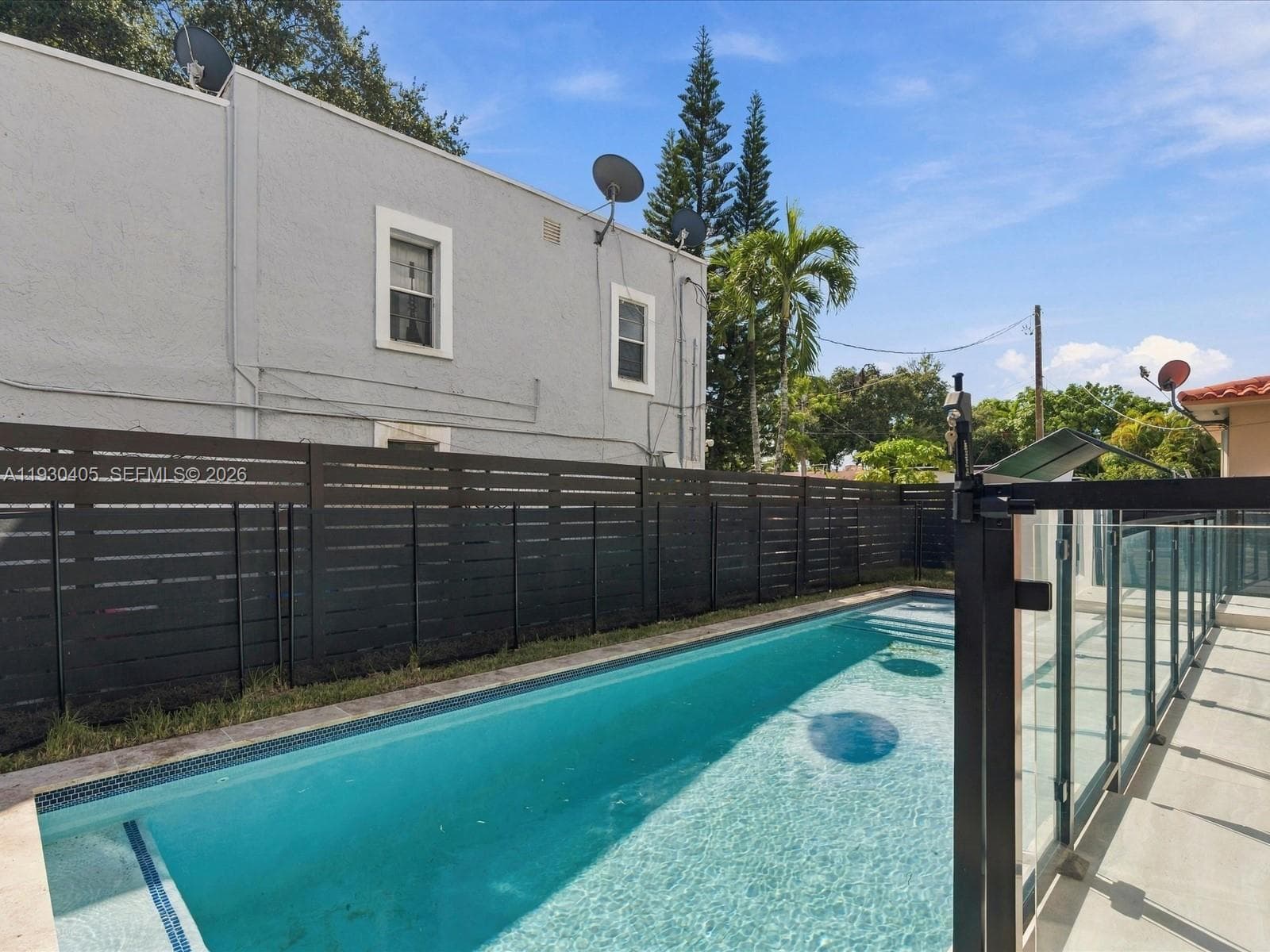 Rectangular swimming pool featuring a tile border, complemented by a horizontal slat privacy fence and a glass panel safety railing